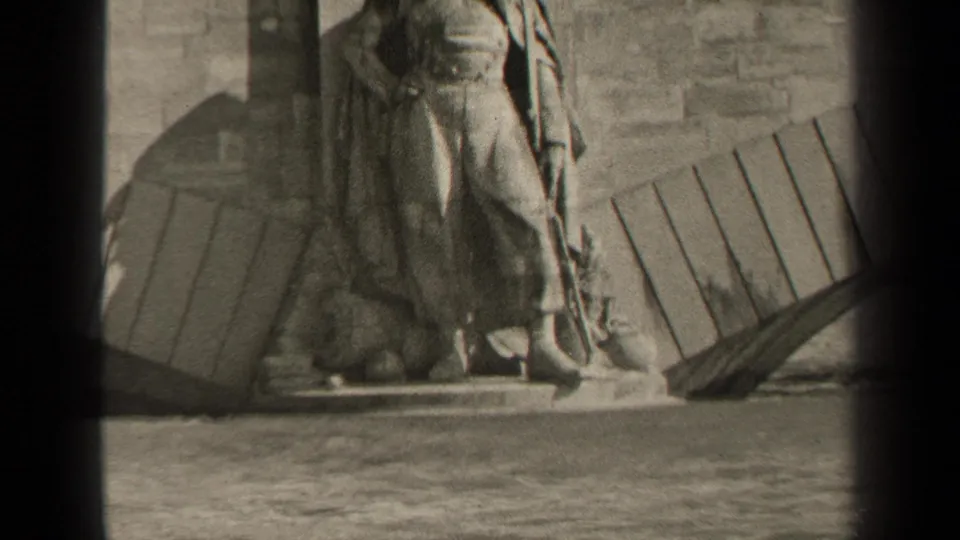 1947 Paris home-movie frame showing the lower part of a large stone statue near the river, with masonry and wooden planks nearby.