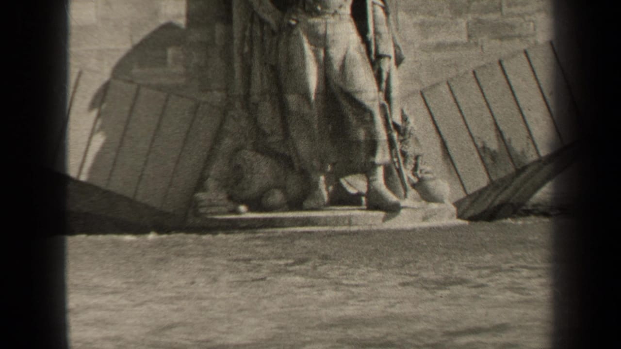 1947 Paris home-movie frame showing a weathered stone statue base, rough wall, timber elements, and water in the foreground.