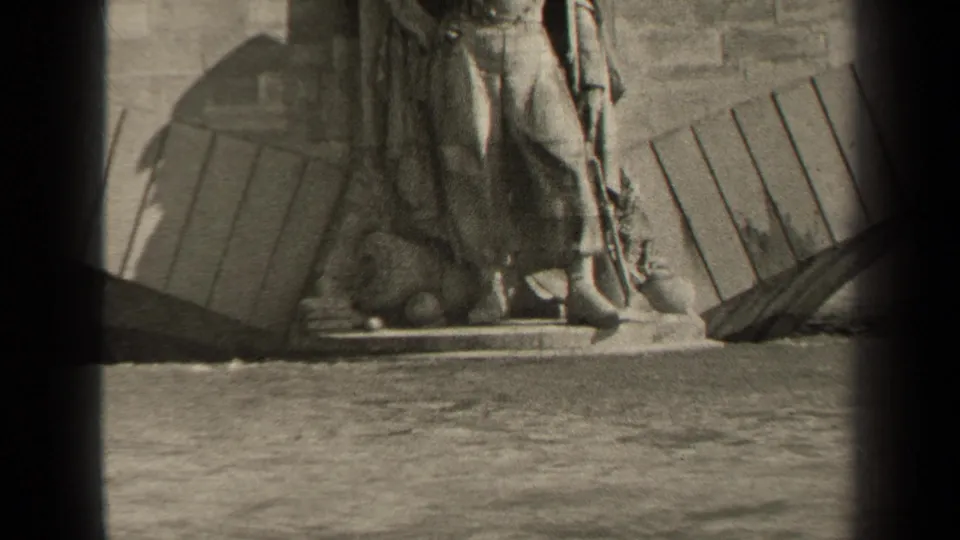 1947 Paris home-movie frame showing a weathered stone statue base, rough wall, timber elements, and water in the foreground.