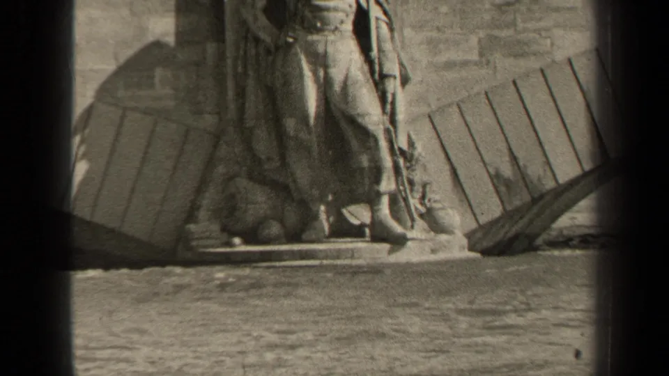 A low 1947 8mm frame holds on a stone figure near water, with wall texture, timber pieces, and heavy film borders visible.