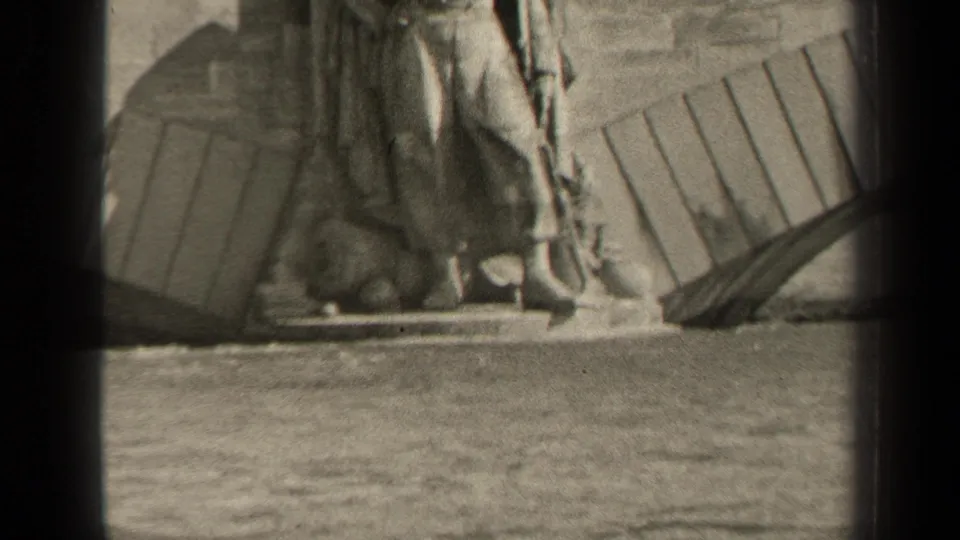 Soft, grainy 8mm frame from 1947 Paris showing the same waterside stone monument with waves moving in front.