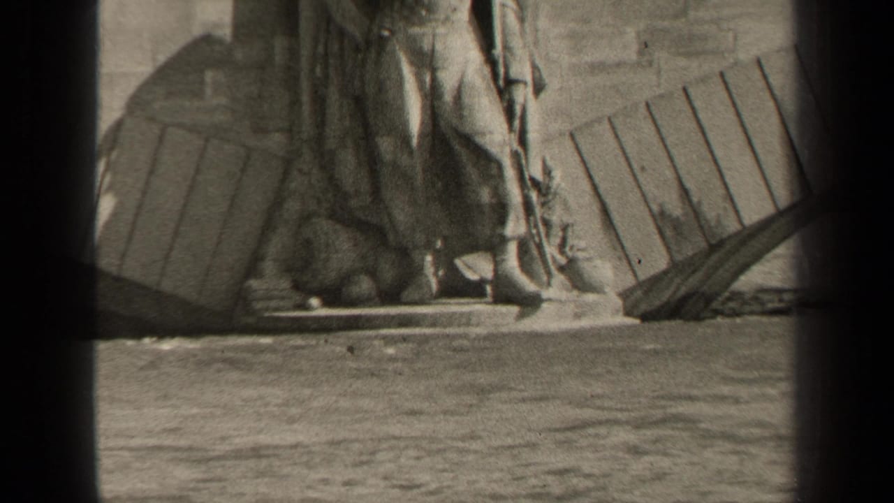 1947 Paris home-movie frame showing the lower part of a monumental statue on a stone base beside water.
