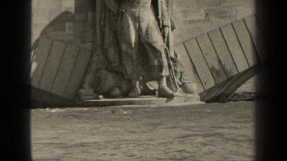 1947 Paris home-movie frame showing the lower part of a monumental statue on a stone base beside water.