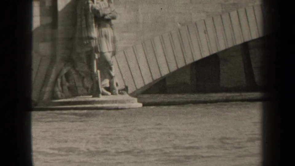 1947 Paris 8mm frame showing the monument base, water, and a curved architectural form behind the statue.