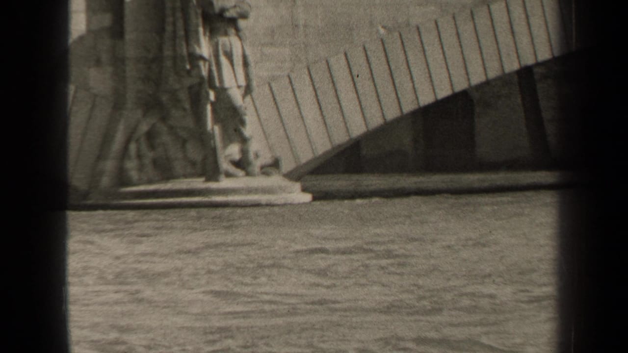 1947 Paris 8mm frame showing a stone statue base near rippling water and a curved slatted structure in the background.