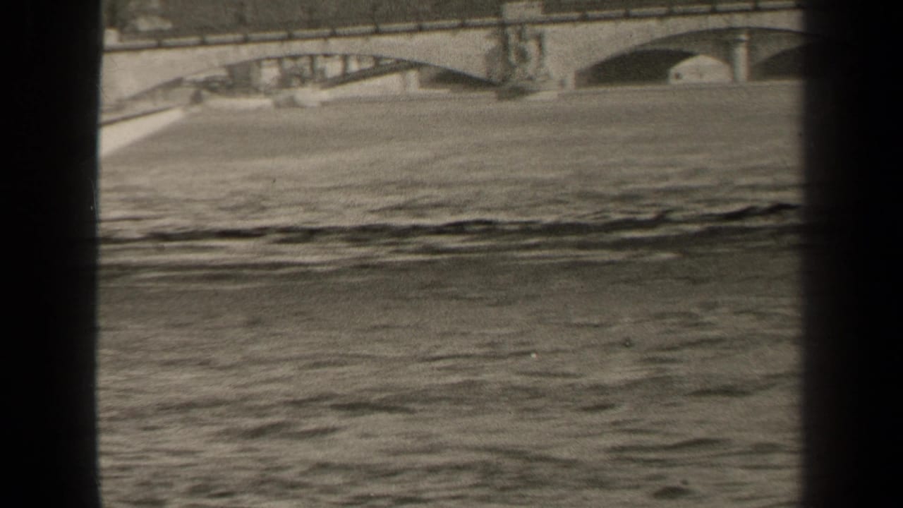 1947 Paris home-movie frame showing rippling river water, a stone bridge and the far riverbank through dark 8mm gate edges.