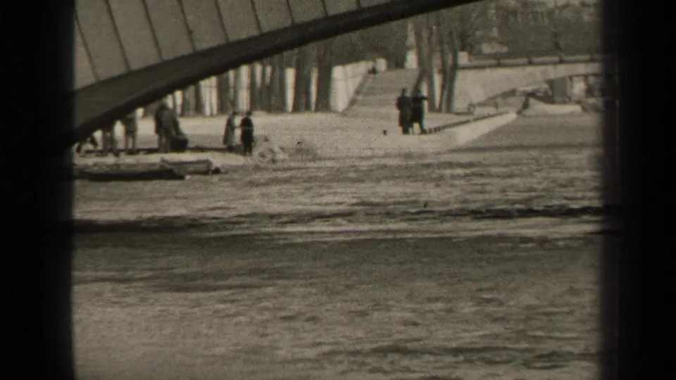 Paris 1947 home-movie frame with a bridge sweeping over the embankment and several distant people near the water.