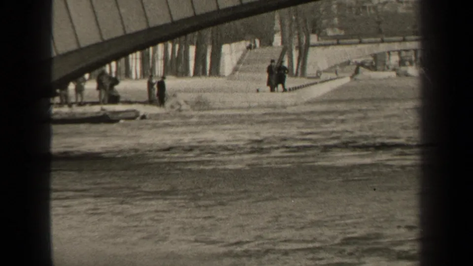 1947 Paris riverside frame with textured water, a bridge span and distant pedestrians along the far embankment.