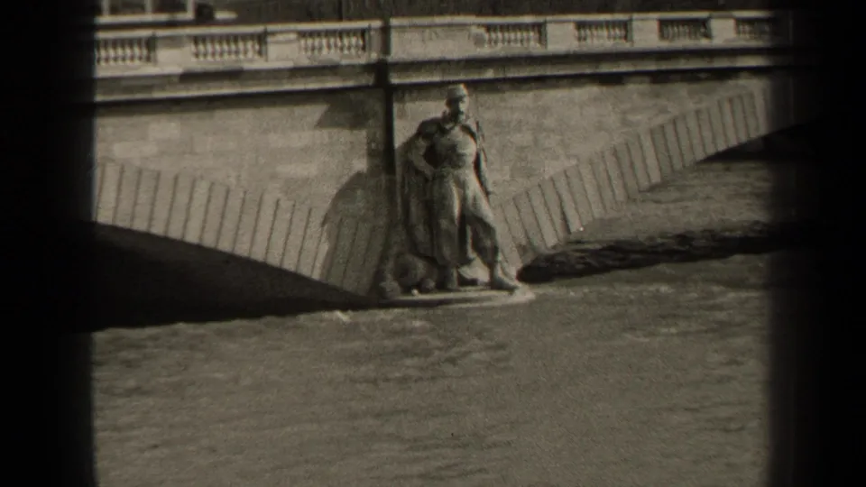 1947 Paris home-movie frame showing a riverside soldier-like statue, stone bridge railing, arch shadow, and water below.