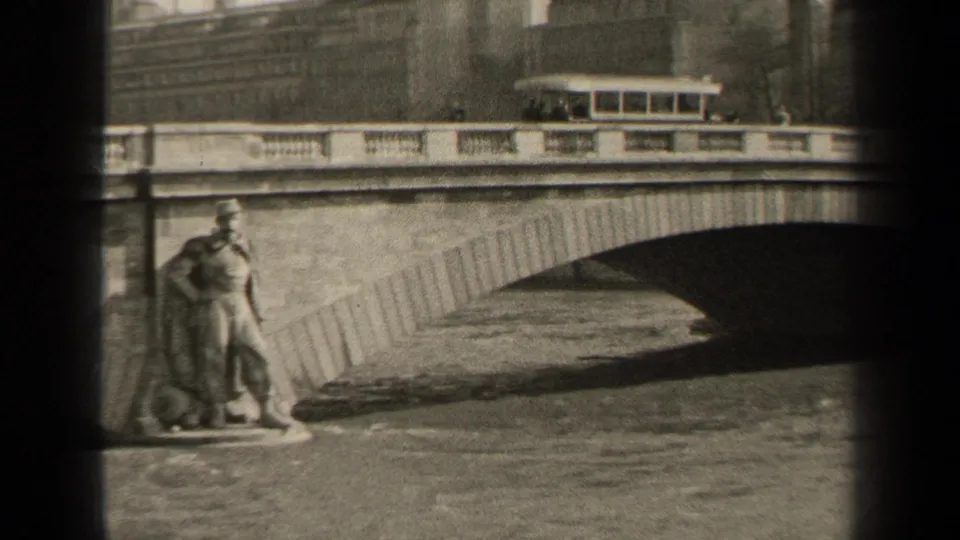 1947 Paris 8mm frame with a bus on the bridge, distant buildings, a soldier-like statue, and water beneath the arch.
