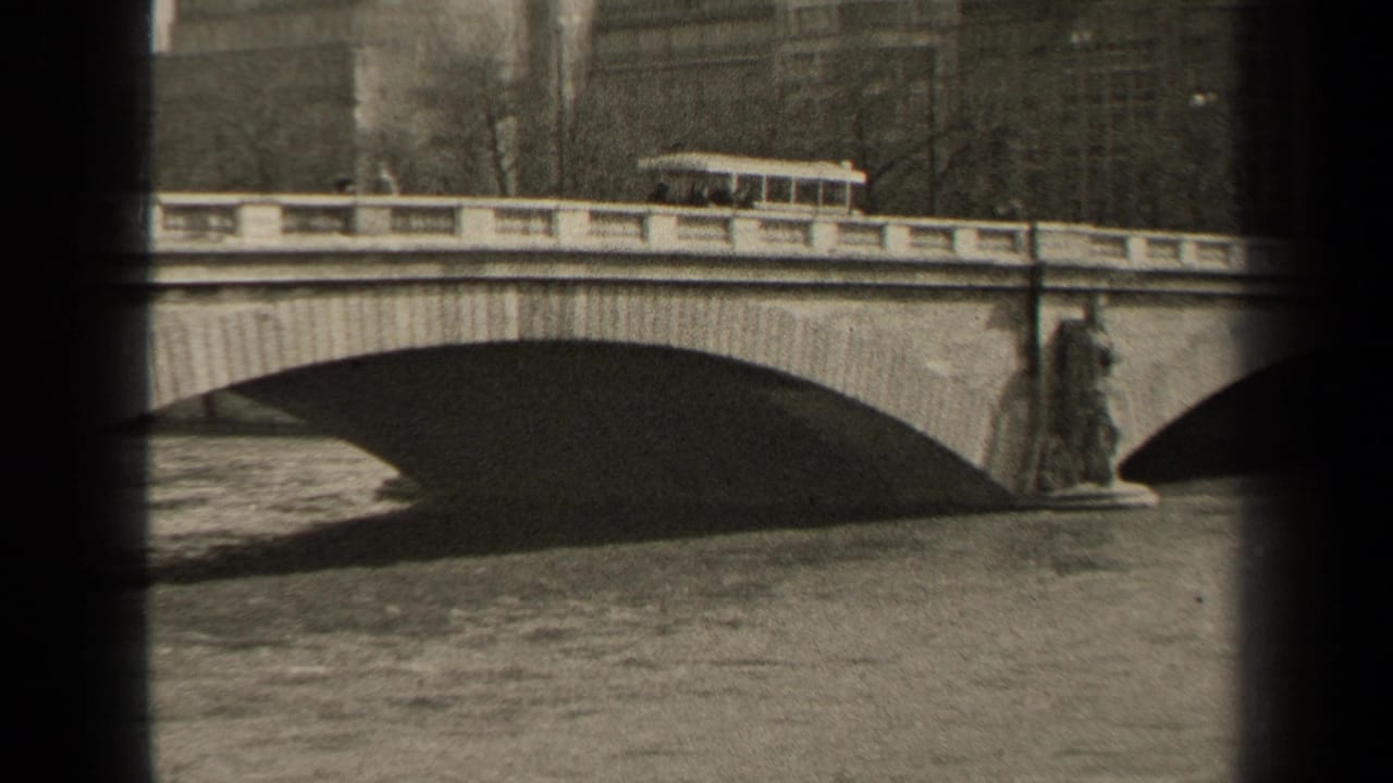 Trolley on bridge with a large arch and river below.