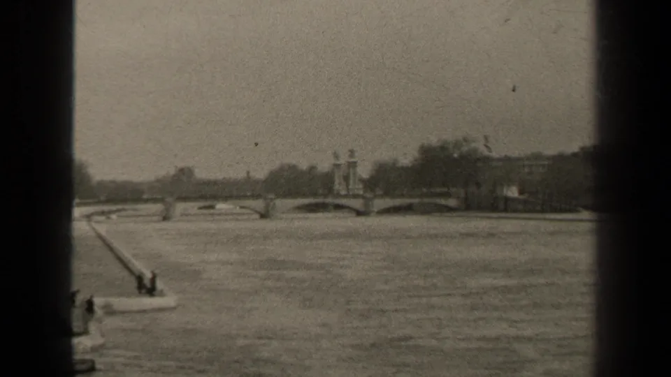 Vintage 8mm Paris frame showing the river, arched bridge, central pier ornament, distant trees, and dark vertical film border.