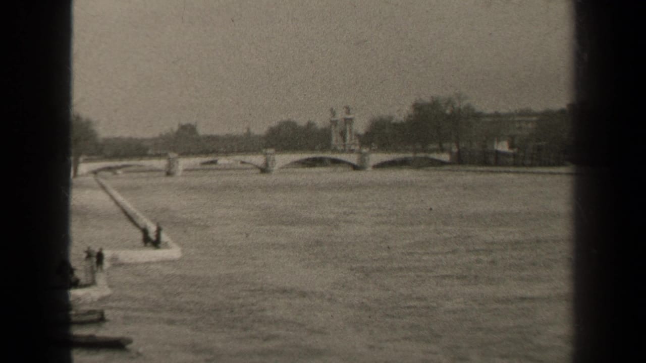 1947 Paris home-movie frame showing a wide river, arched stone bridge, riverside ramp, small boat, and distant figures.