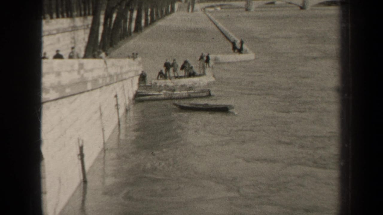1947 Paris riverside view with several people on or near a moored vessel, a small boat nearby, and a stone embankment running along the water.