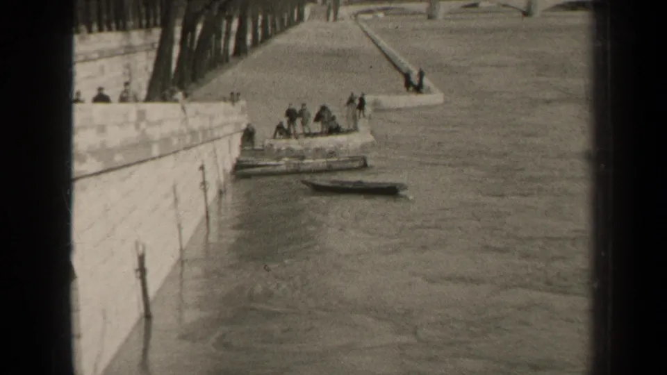 1947 Paris riverside view with several people on or near a moored vessel, a small boat nearby, and a stone embankment running along the water.