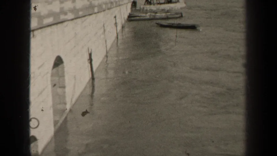 1947 Paris riverside frame with a stone quay, arched wall opening, moored boats, and distant people partly near the top of the shot.