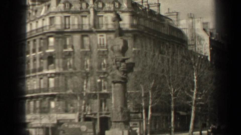 1947 Paris street scene with a monument in front of apartment buildings, bare trees, a truck, and pedestrians in soft black-and-white 8mm footage.