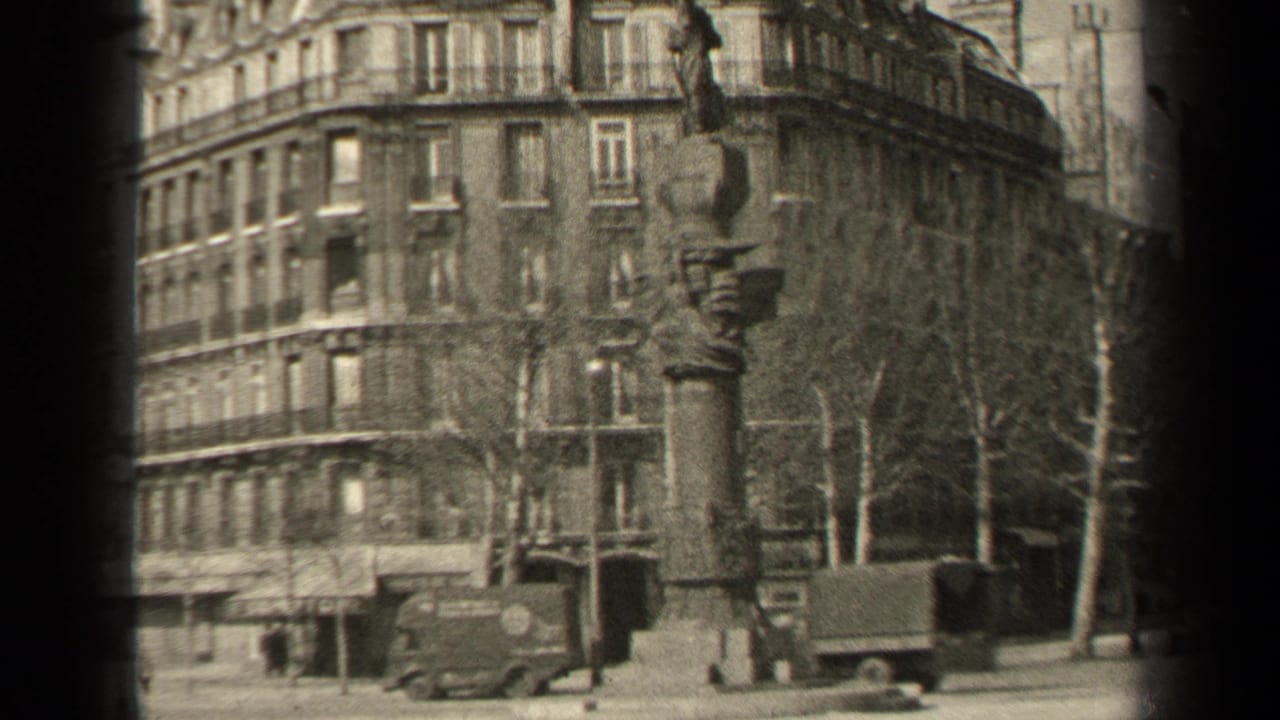 1947 Paris street view with a stone column monument, multi-story apartment facade, bare trees, and older vehicles near the curb.