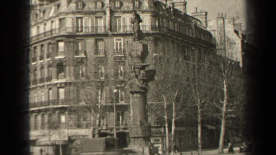 1947 Paris exterior showing a tall stone monument before a residential facade, with leafless trees and older vehicles along the street.