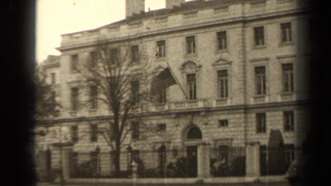 1947 Paris exterior view of a formal stone building with a flag over the entrance, leafless tree, iron fence, and early cars nearby.