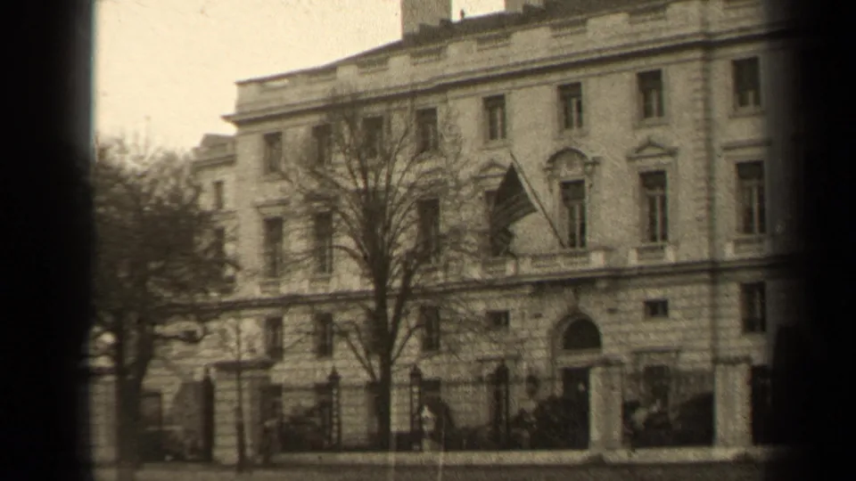 1947 Paris 8mm frame with a tilted handheld view of the classical building, flag, bare tree, iron fence, and street edge.