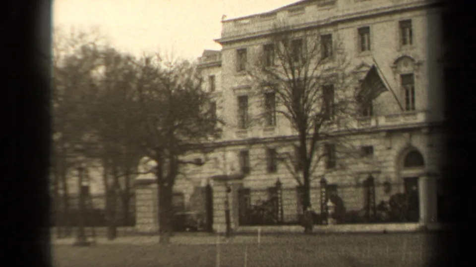 Paris 1947 exterior view of a classical facade with a blowing U.S. flag, bare trees, fence, and small pedestrians.