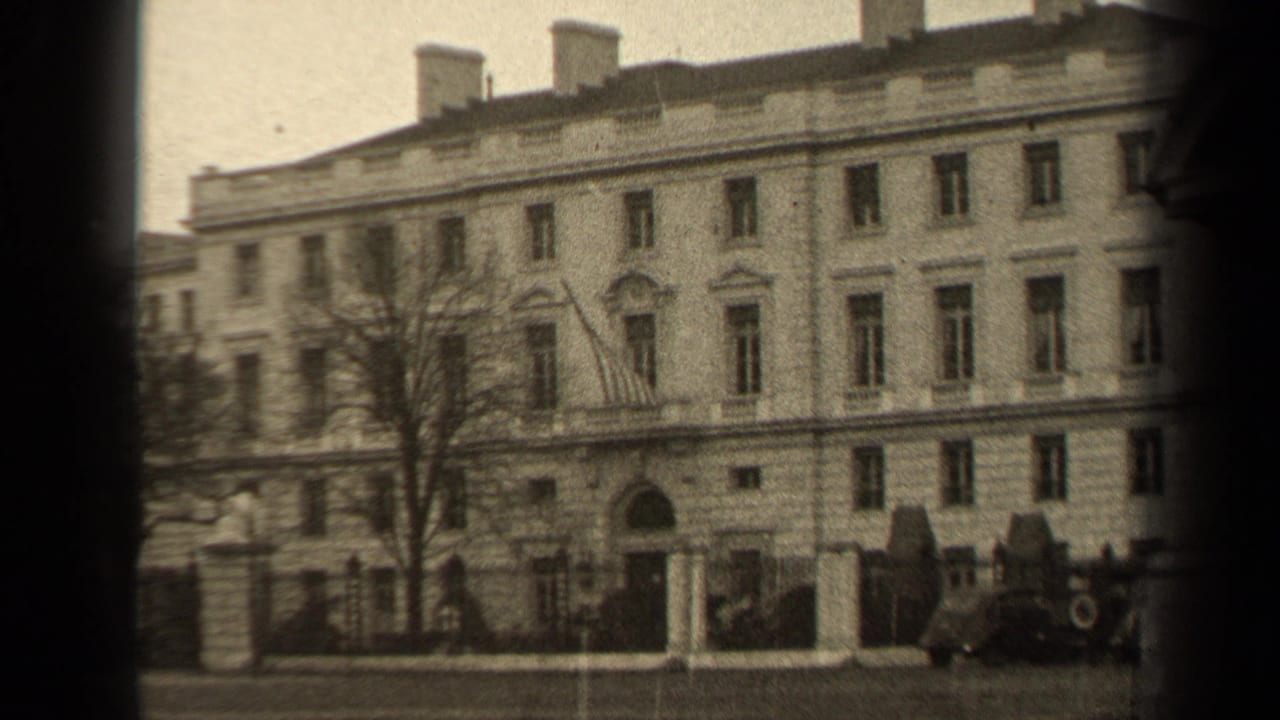 1947 Paris 8mm frame showing a grand stone facade behind a gate, with an American flag above the entrance and cars at the curb.