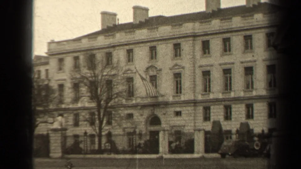 1947 Paris 8mm frame with a closer handheld view of the gated stone facade, flag over the entrance, bare tree, and period automobiles.