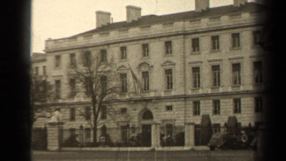 1947 Paris exterior view of a formal stone building with tall windows, an arched entrance, fencing, and street-side cars.