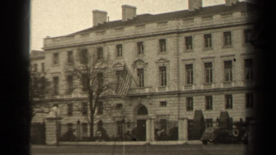 1947 Paris frame showing the building entrance area, a flag by the facade, bare branches, and cars along the street.