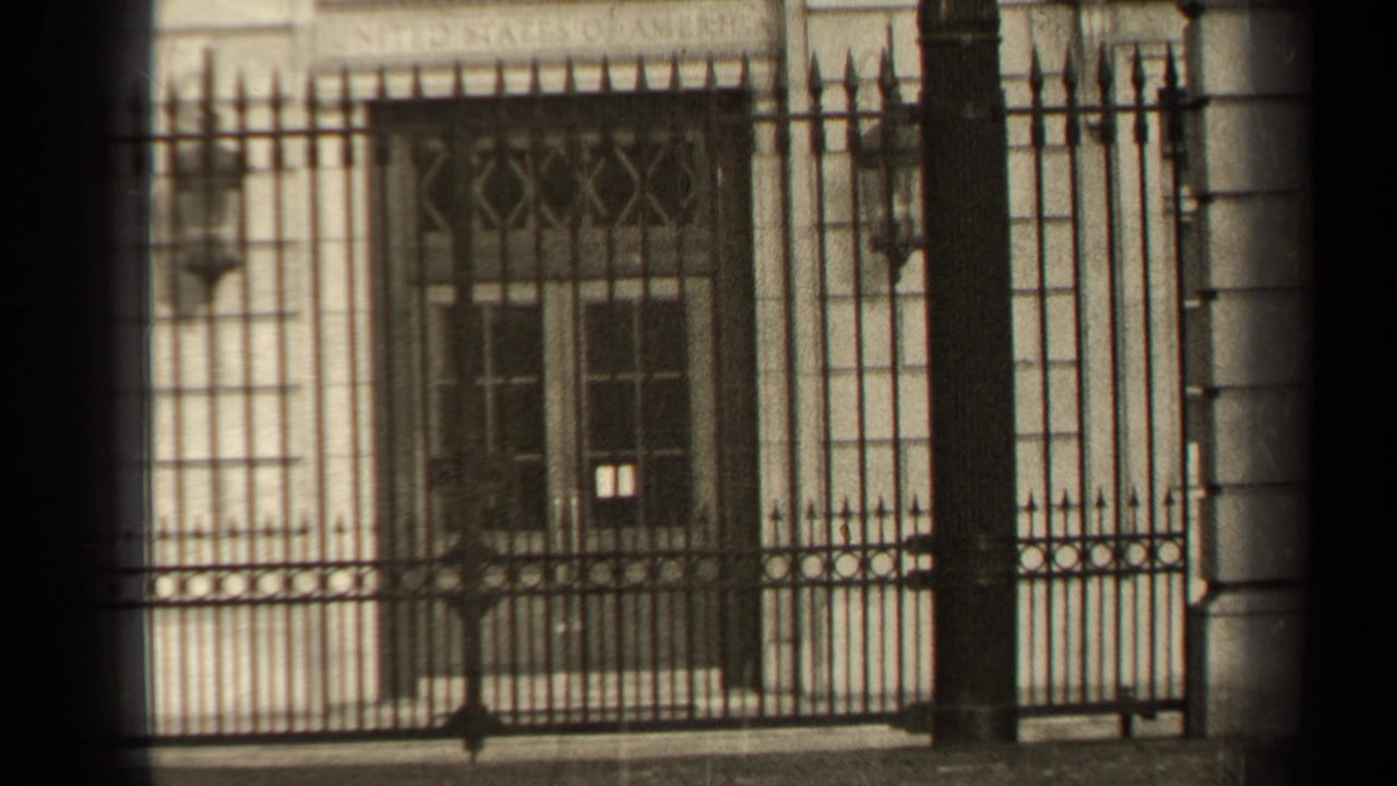 1947 Paris home-movie frame showing a pale stone building behind ornate iron railings, with barred windows and soft winter light.