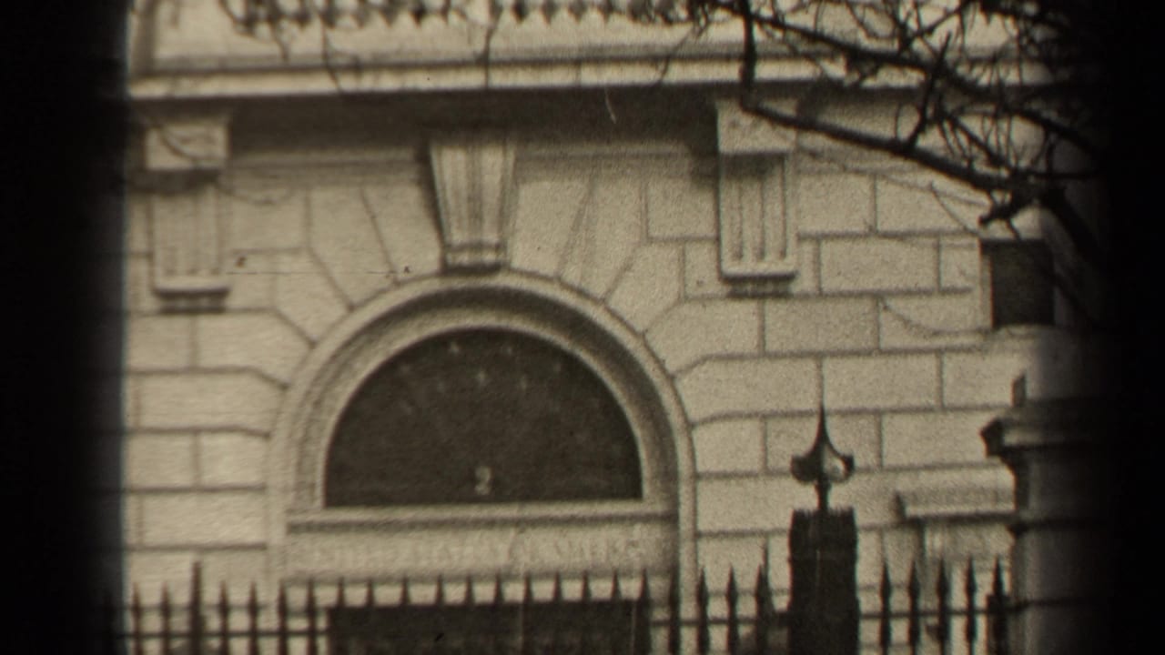 1947 Paris frame showing an arched entrance, pale masonry, iron fence, and bare branches across the upper right.