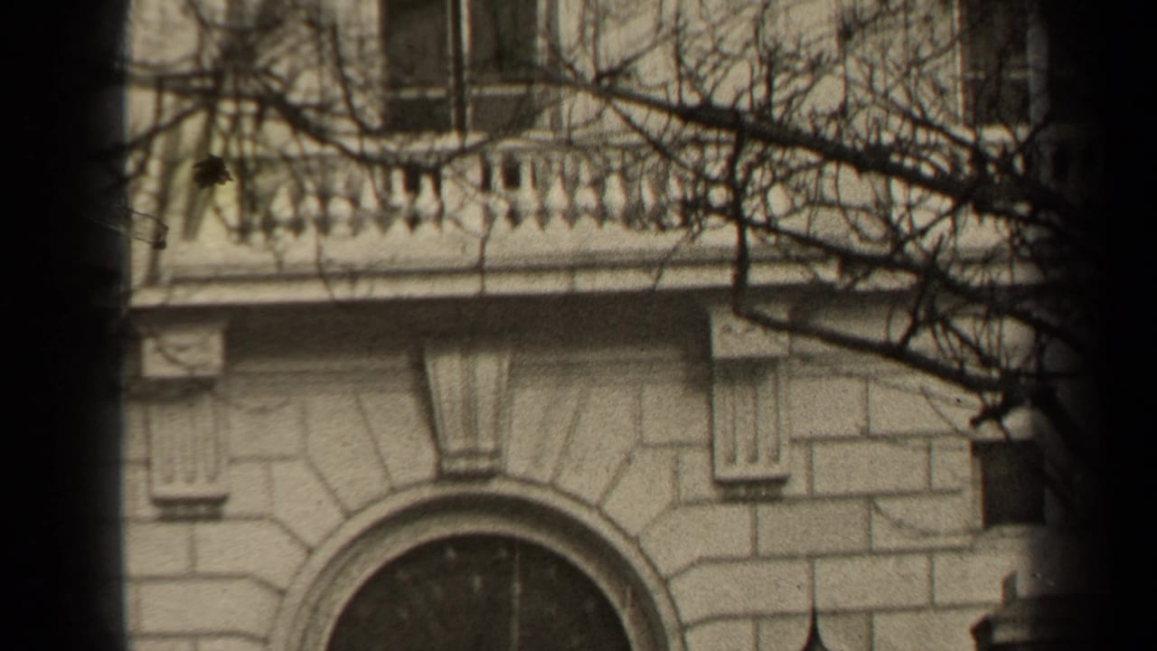 1947 Paris 8mm frame showing a pale stone facade, arched window, balcony balustrade, bare branches, and dark vertical foreground bands.