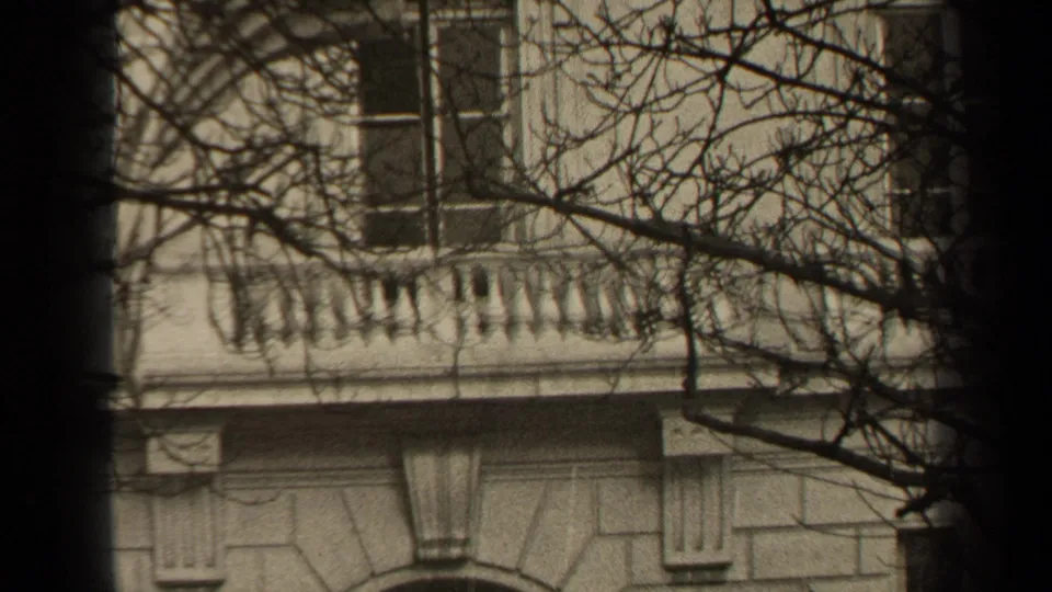 1947 Paris 8mm frame of an upper building facade with rectangular windows, a balustraded balcony, bare branches, and a dark vertical foreground band.