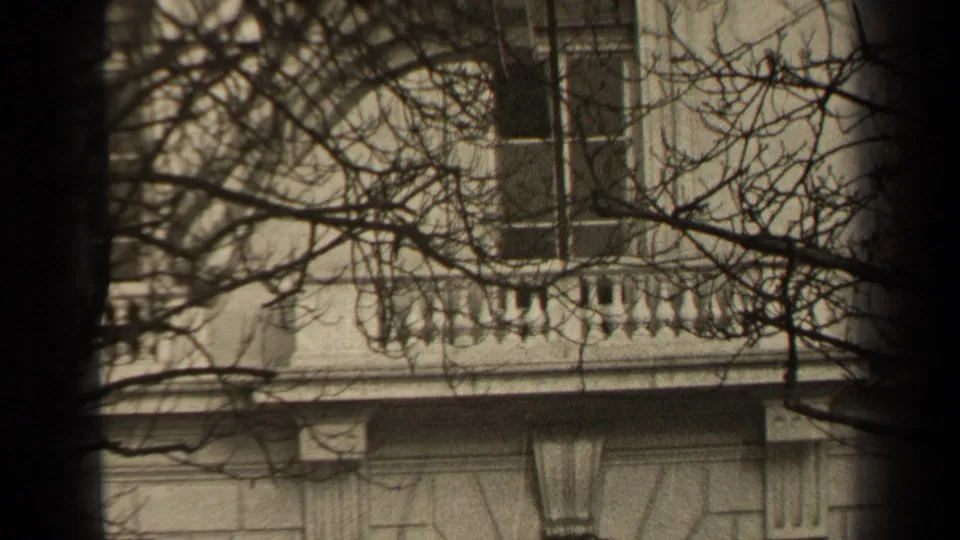 1947 Paris 8mm frame showing a close view of a stone facade, rectangular window, balustrade, decorative masonry, and dense bare branches.