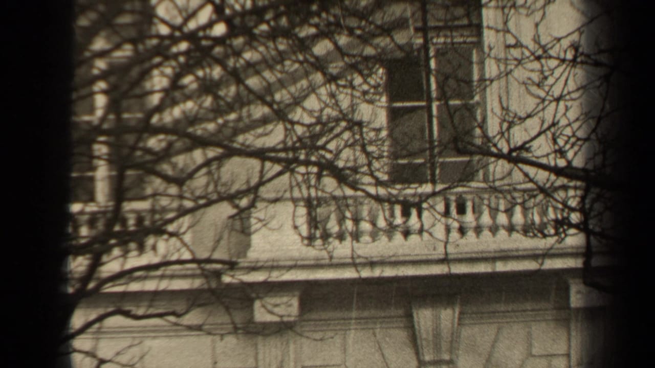 1947 Paris 8mm frame showing a stone eagle statue near a classical building, seen through branches and dark film-edge vignetting.