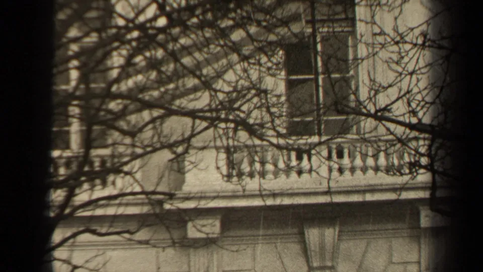 1947 Paris 8mm frame showing a stone eagle statue near a classical building, seen through branches and dark film-edge vignetting.