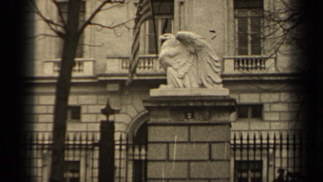 Stone eagle on a gate pillar beside an iron fence and classical building facade.