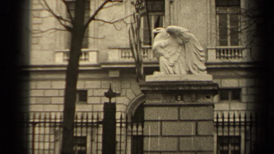 1947 Paris 8mm frame showing a stone eagle on a pillar, an American flag nearby, and a classical building behind iron fencing.