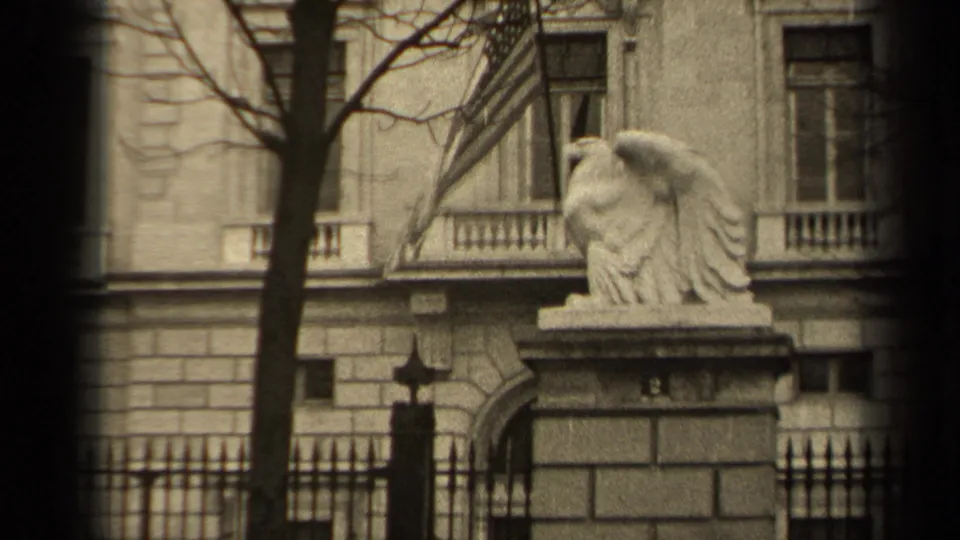 1947 Paris frame with a stone eagle sculpture, iron fence, bare trees, and a multi-story stone facade visible through dark film edges.