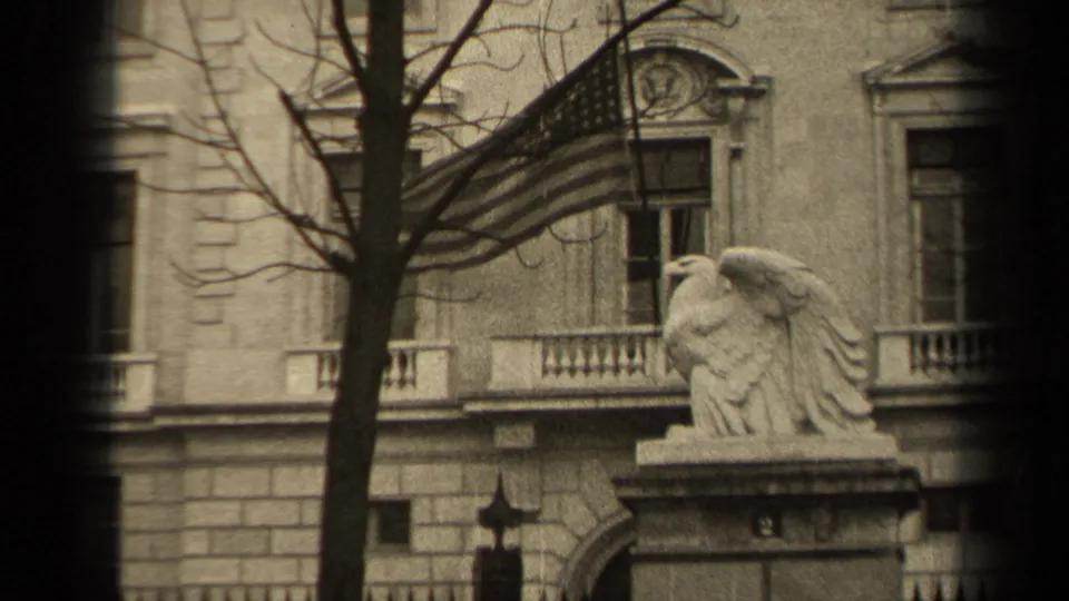 1947 Paris frame with the U.S. flag crossing the upper facade as the stone eagle statue sits below beside a bare tree and iron fence.