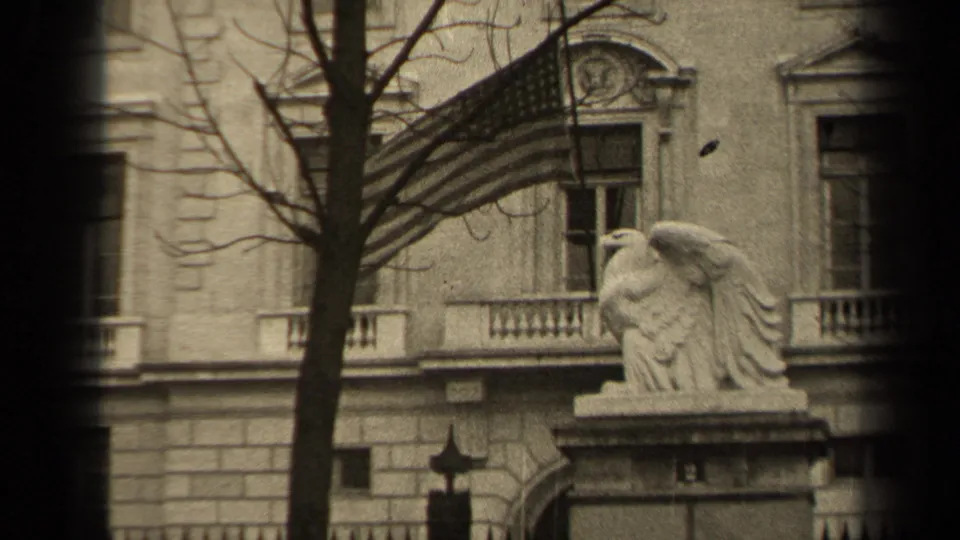 1947 Paris 8mm frame showing a stone facade, American flag, eagle statue, bare tree branches, and a dark vertical film edge.