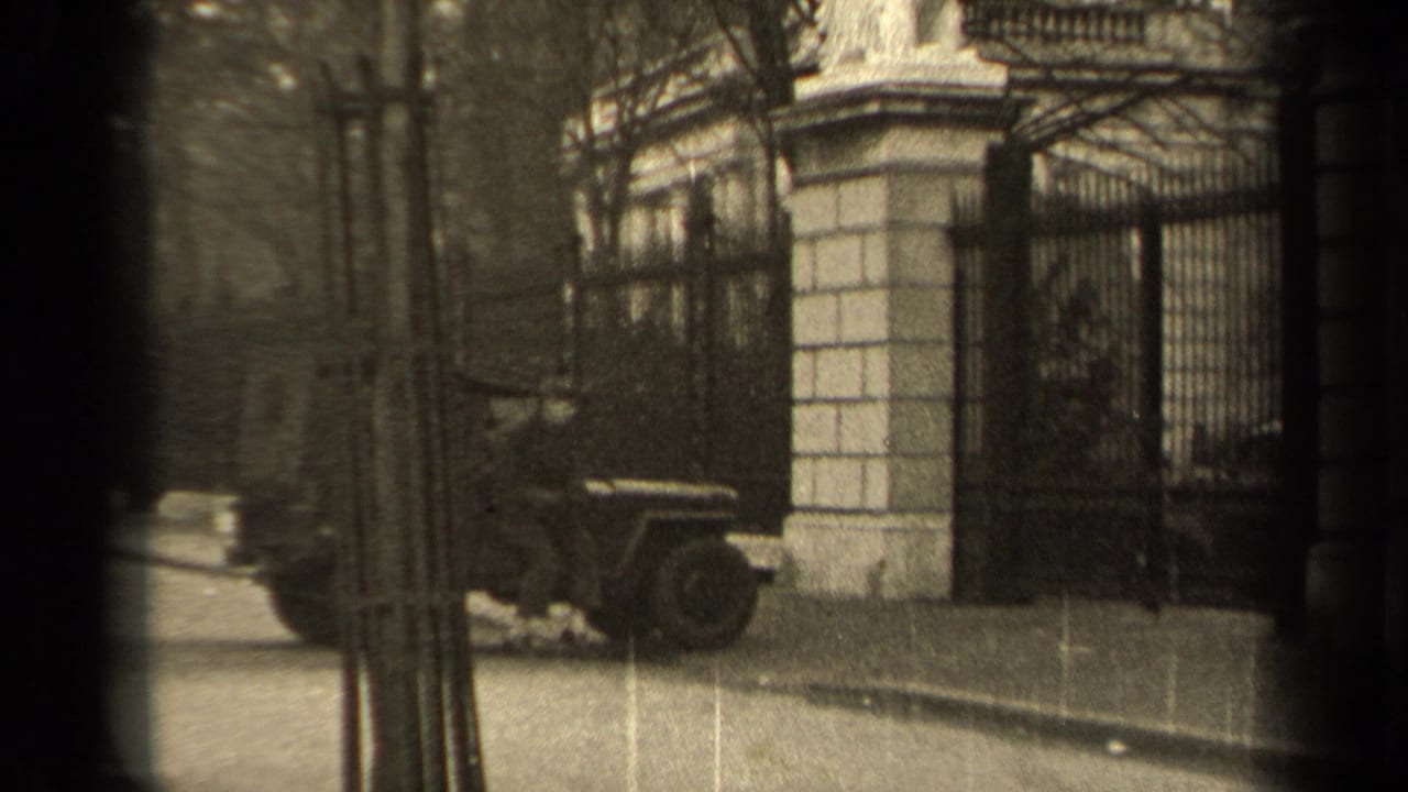 Military-style jeep parked near a wrought-iron gate and stone gateposts on a Paris street.