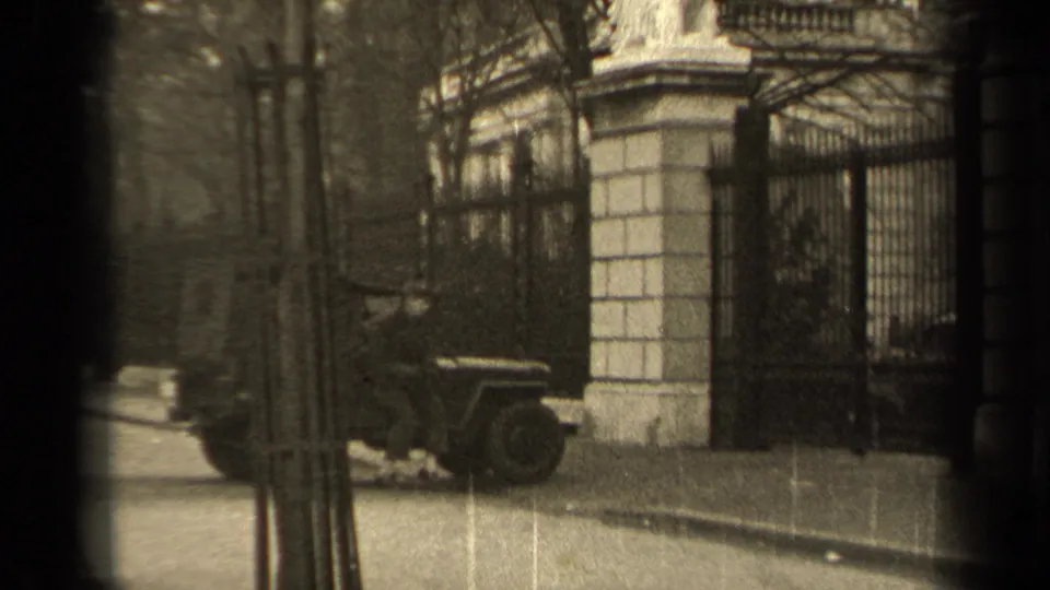 1947 Paris 8mm frame with a military-style jeep beside a wrought-iron gate, stone gateposts, bare trees, and sidewalk.