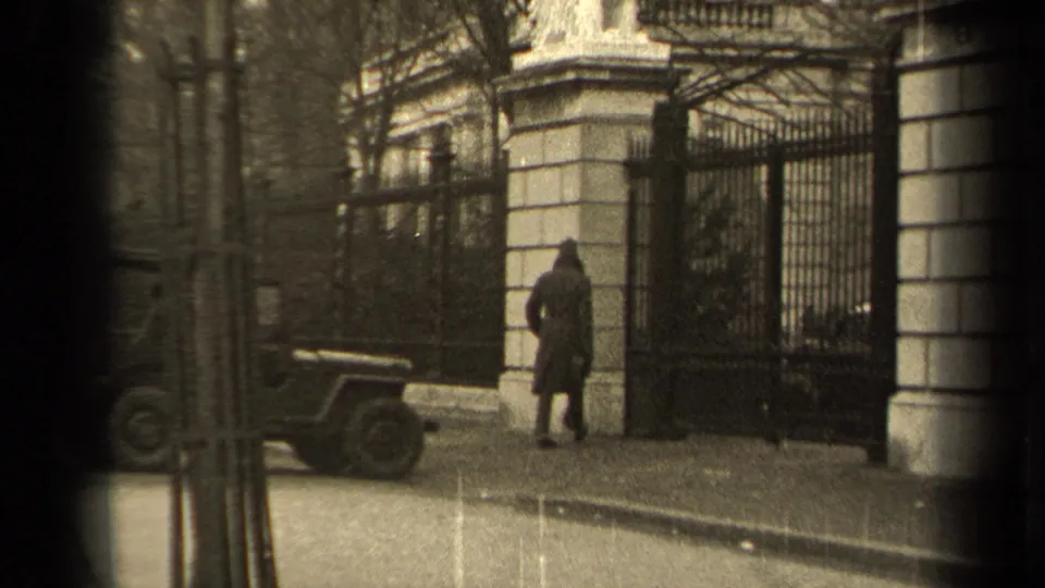 1947 Paris 8mm frame of a man near a formal wrought-iron gate, with a parked military-style jeep and stone gateposts visible.