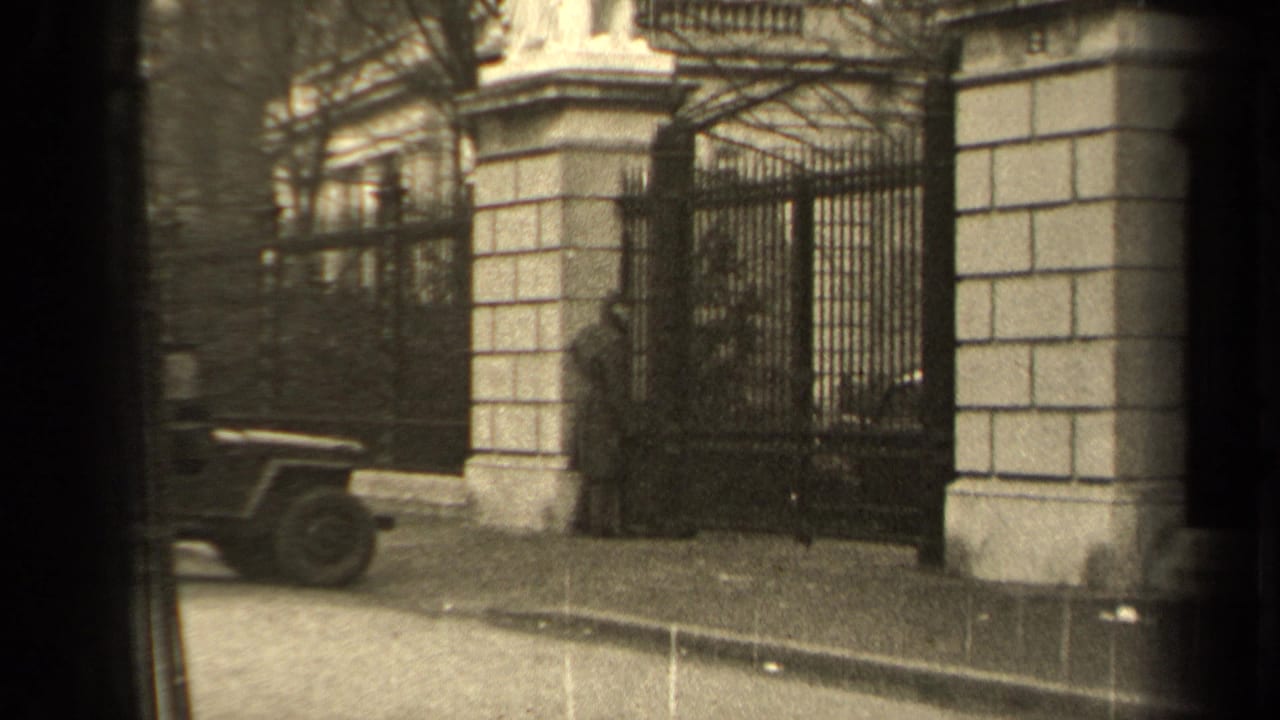 A distant man in a dark overcoat is seen beside the iron gate of a stone building in Paris, France, in 1947 footage.