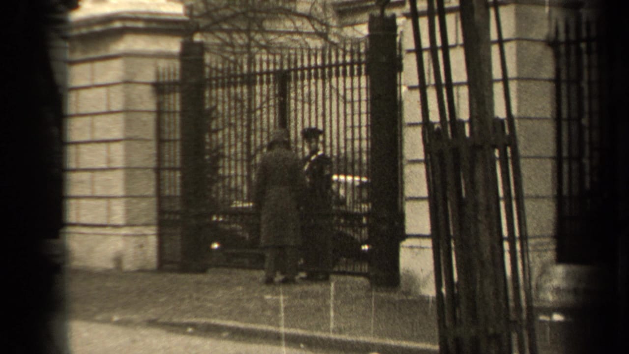Uniformed guard stands by the iron gate as a man presents papers.