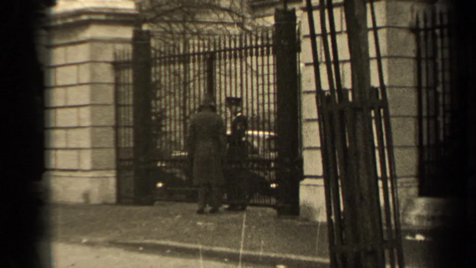 The visitor remains at the gated entrance while the uniformed guard examines or receives papers.