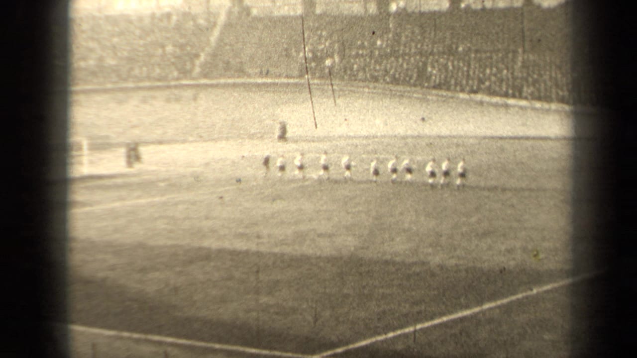 1947 Paris football players appear lined up on the field, filmed from a distant spectator viewpoint in a crowded stadium.