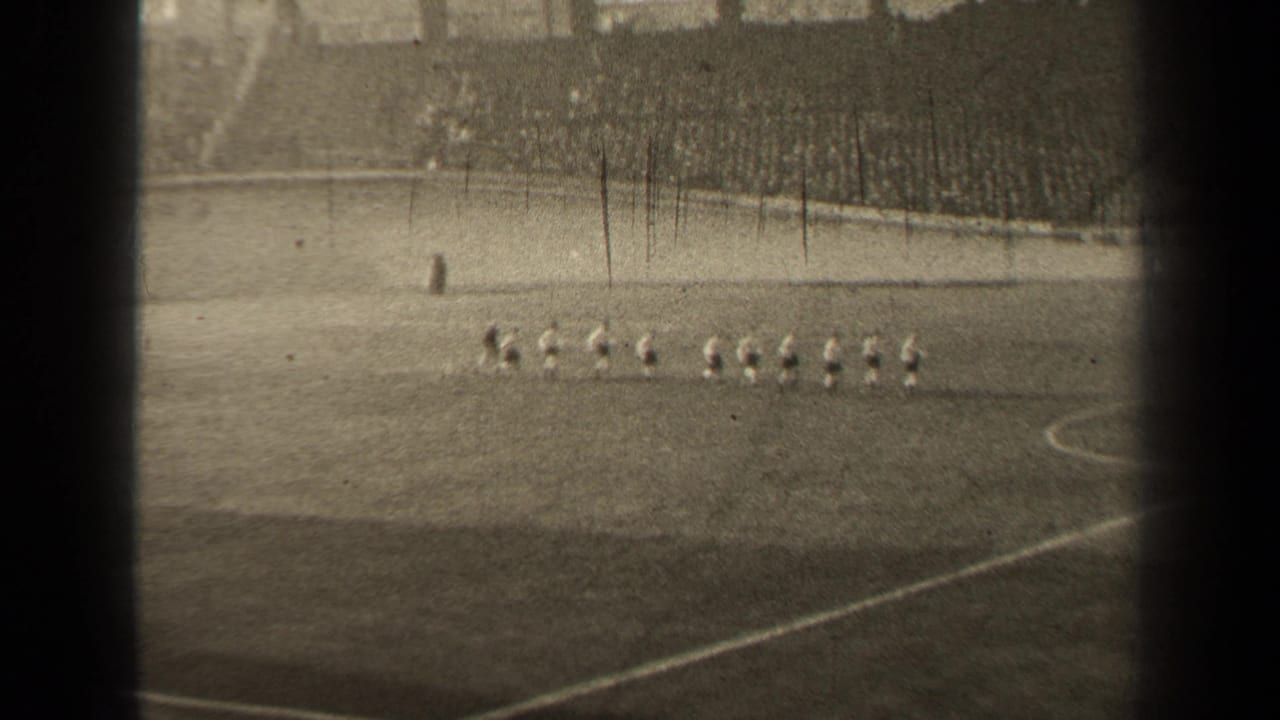 Distant 1947 Paris stadium view showing football players lined up on the pitch before the match continues.